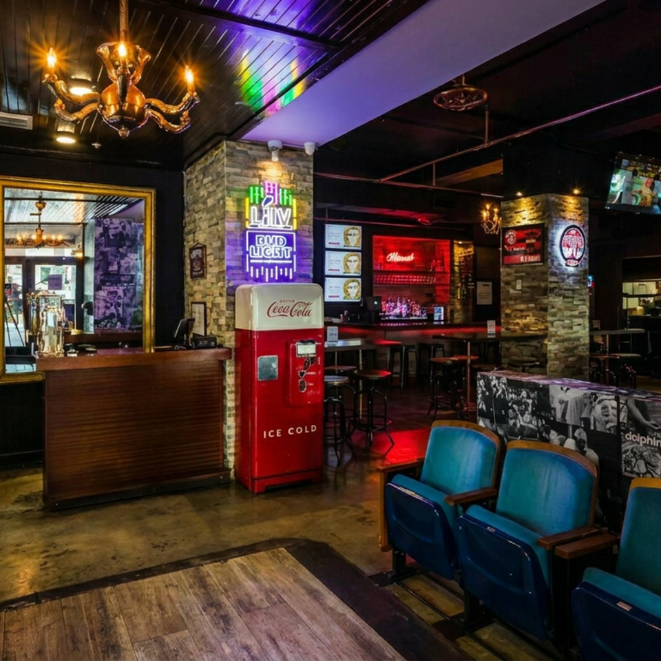 Retro-themed restaurant lounge with leather sofas, theater seats, neon signs, a vintage Coca-Cola cooler, and colorful bar lighting.