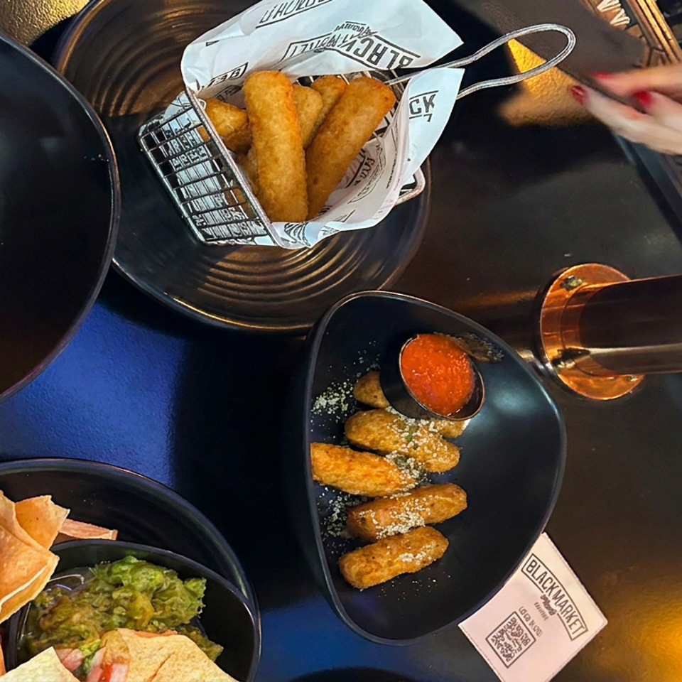 Overhead view of fried appetizers with dipping sauces, tortilla chips, guacamole, and tongs on a Black Market restaurant table.